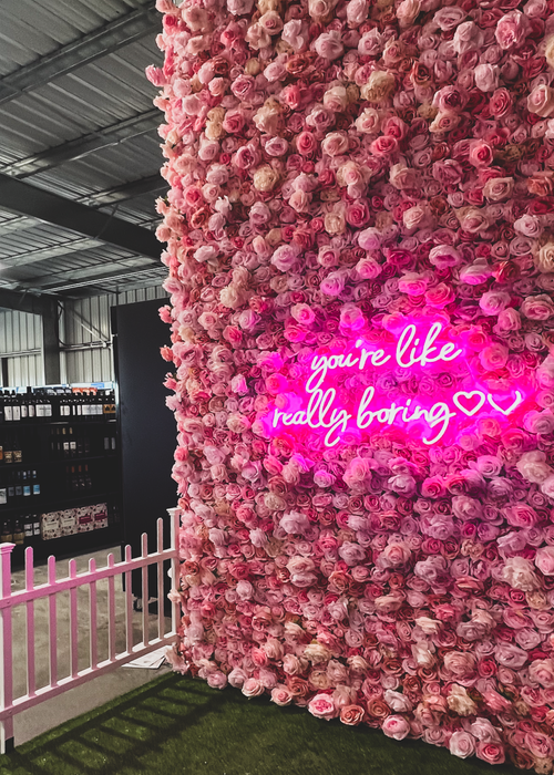 Pink rose flower wall with 'you're like really boring' neon sign