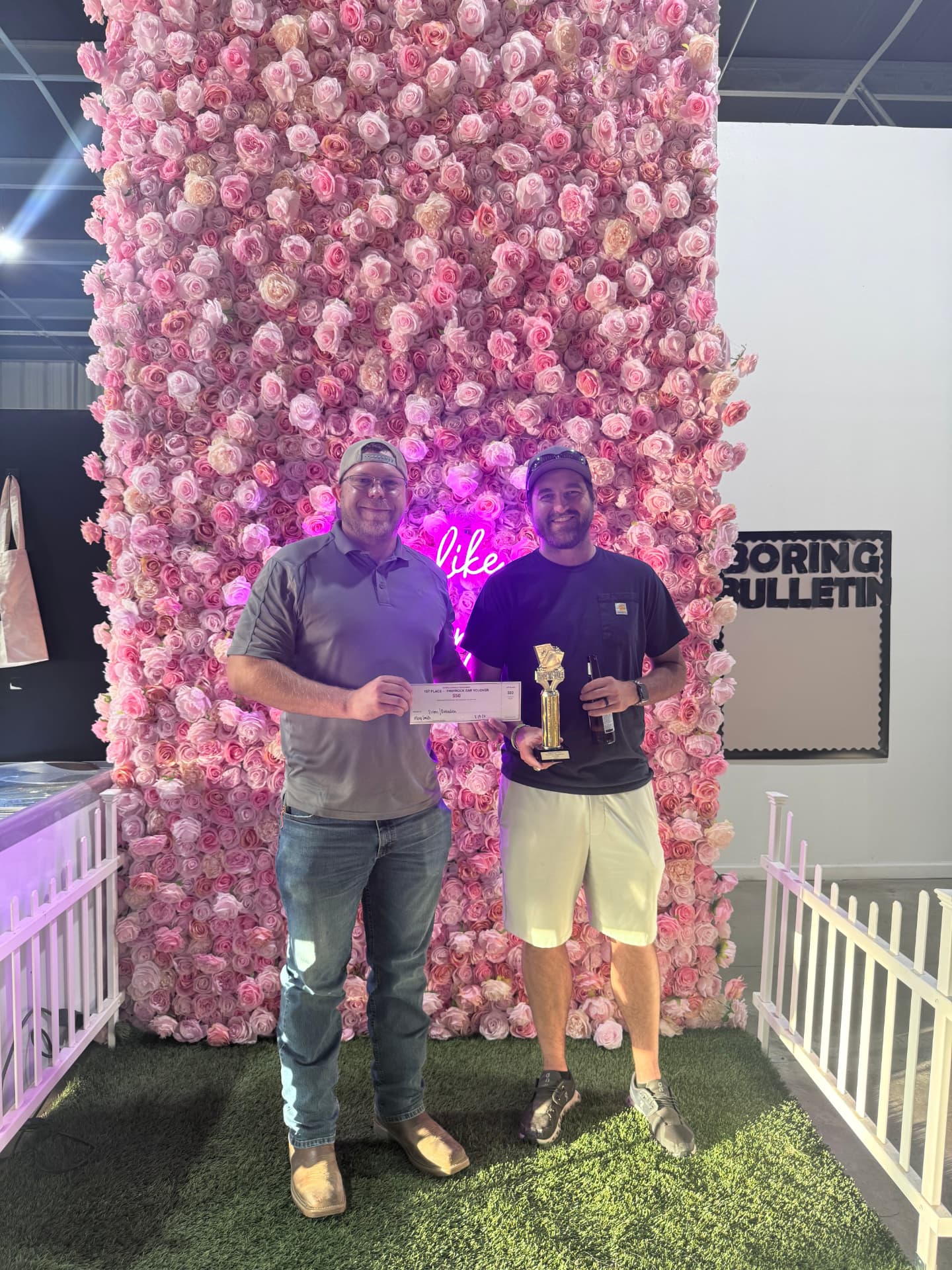 Cornhole tournament winners with their trophy at the pink flower wall